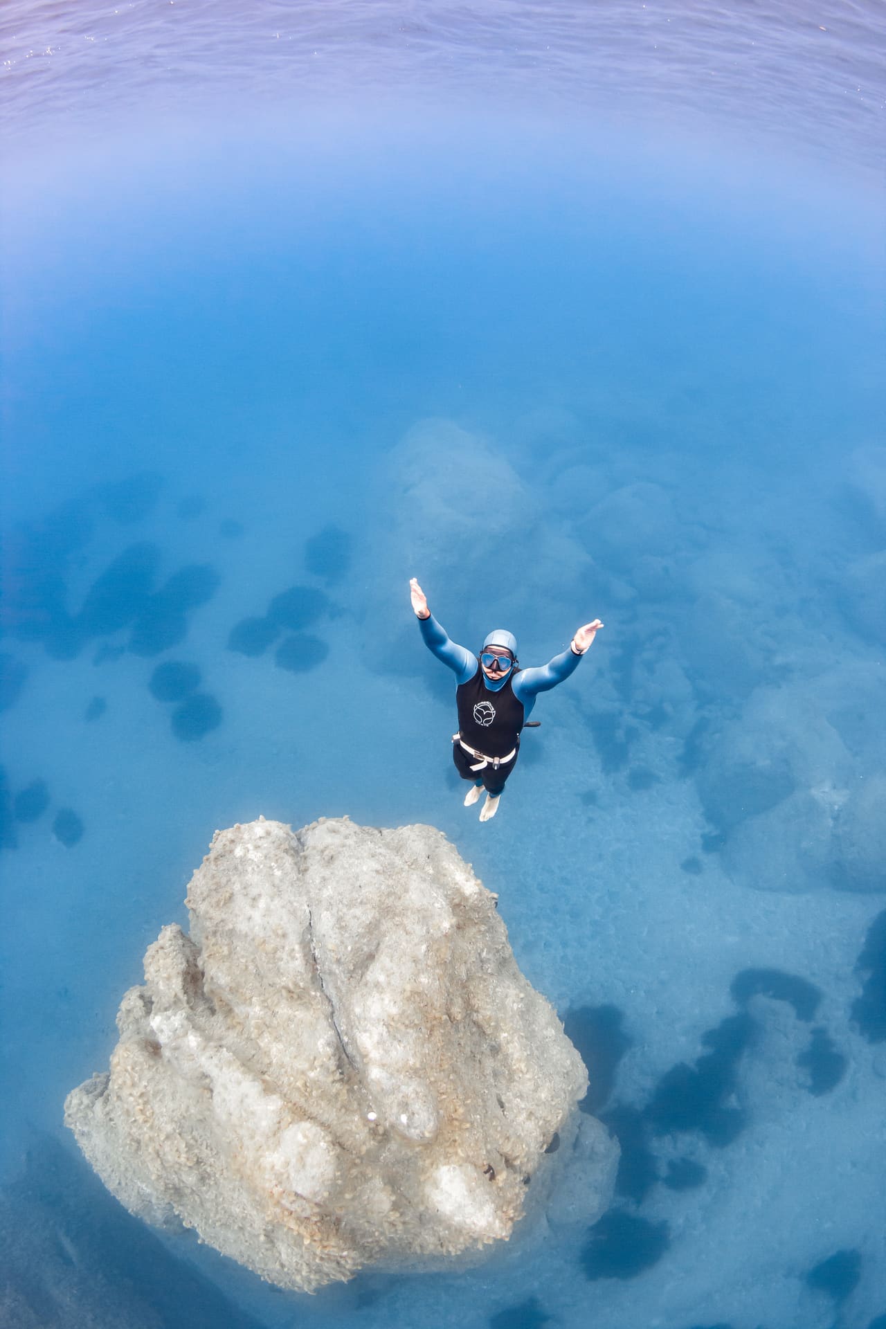 Freediver ascending over a rock formation in clear blue water
