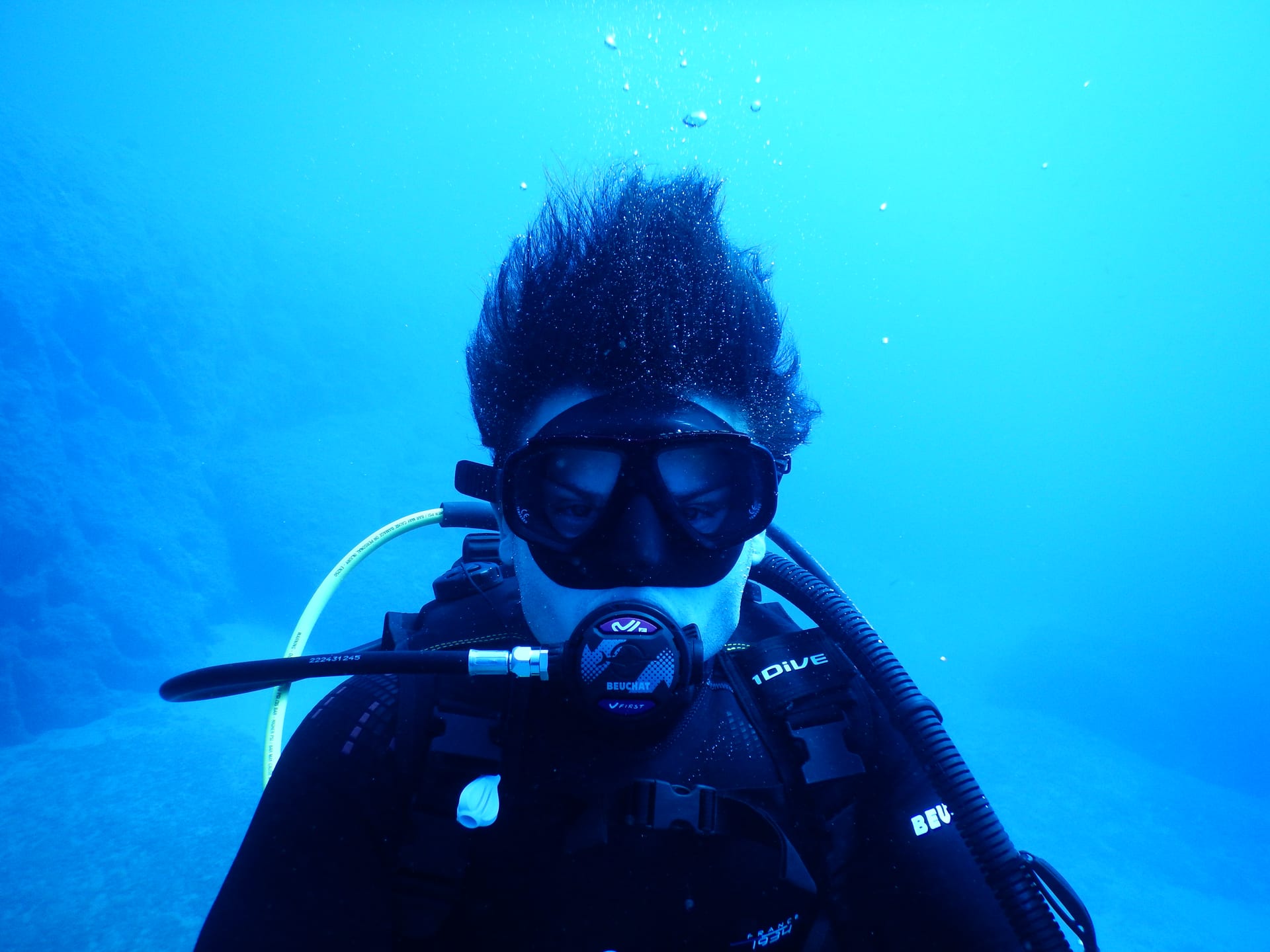 A first-time diver kneeling on the seabed giving the OK sign